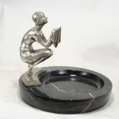 A silver statue sitting on top of a black marble ashtray.